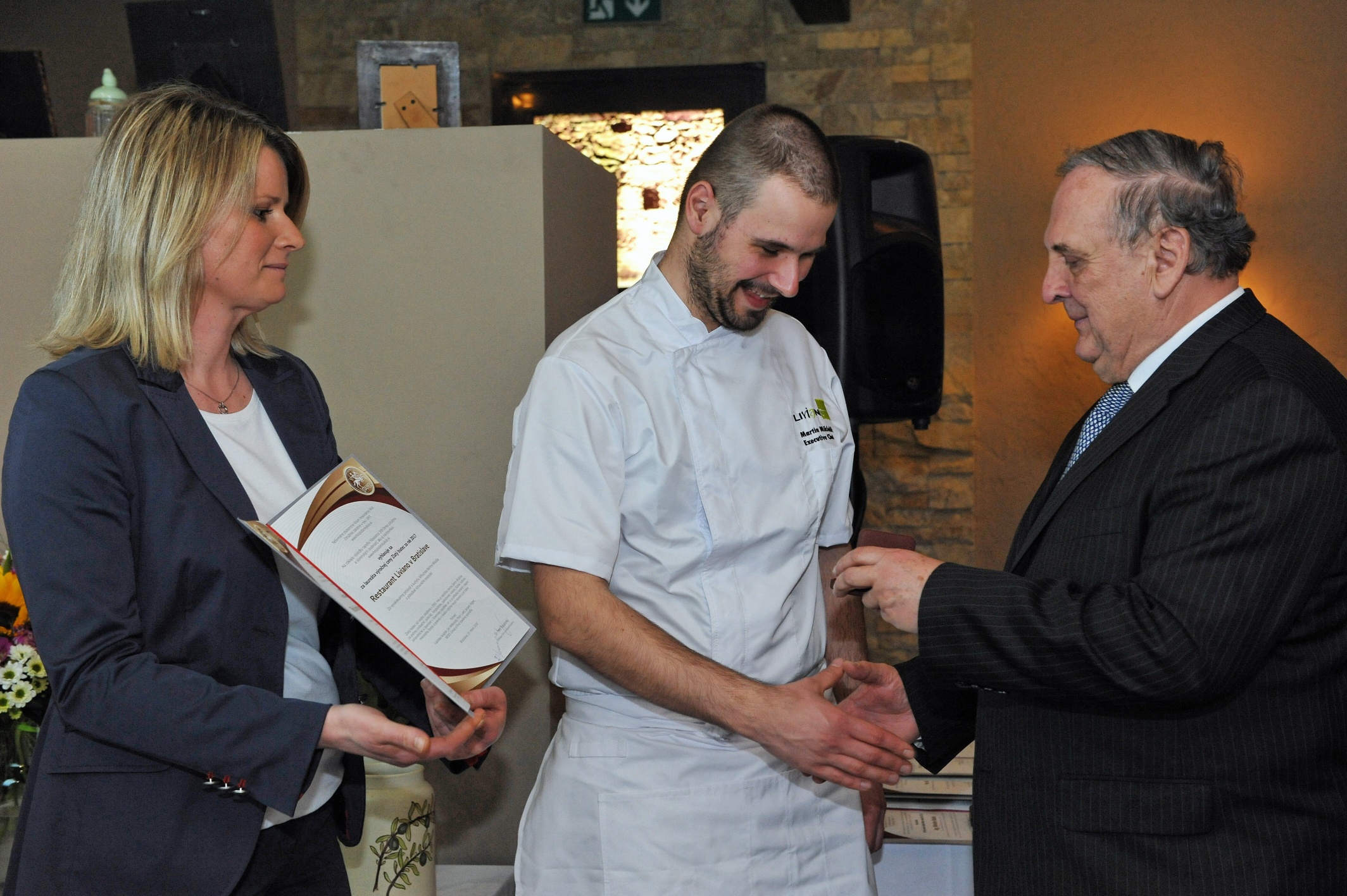 Šéfkuchár Restaurantu Liviano M. Miklošík preberá od P. Mihóka Zlatý biatec a riaditeľka tohto zariadenia A. Husáková s diplomom, ktorý potvrdzuje druhú pozíciu medzi nominovanými.